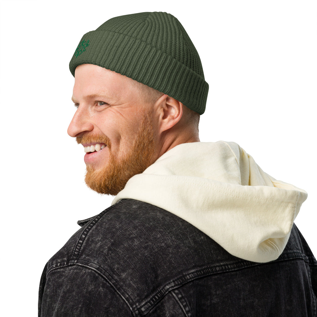 Man wearing a green beanie with red text and a white hoodie peeking out from under a black jacket on a white background