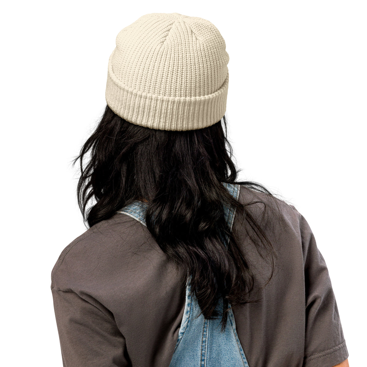 Person wearing a beige beanie and denim overalls on a white background