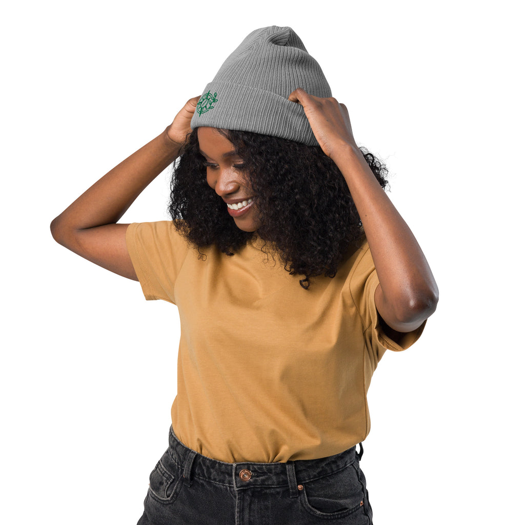 Person wearing a mustard yellow shirt and black pants, holding a gray beanie above their head on a white background