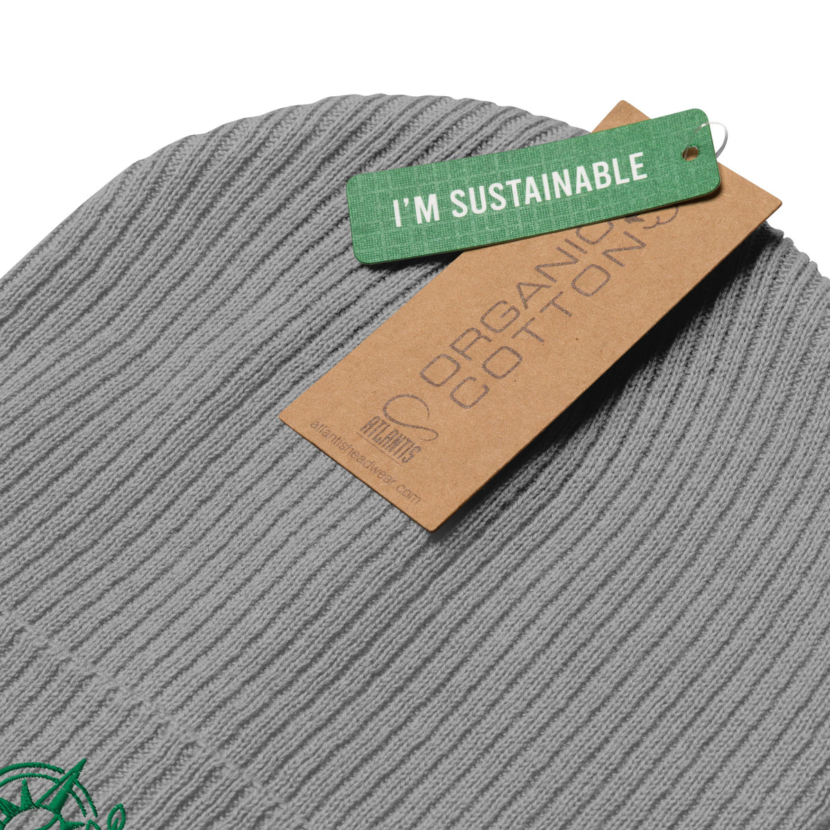 Close-up of a gray ribbed knit beanie with a brown paper tag reading 'ORGANIC COTTON' and a green tag reading 'I'M SUSTAINABLE' on a white background.
