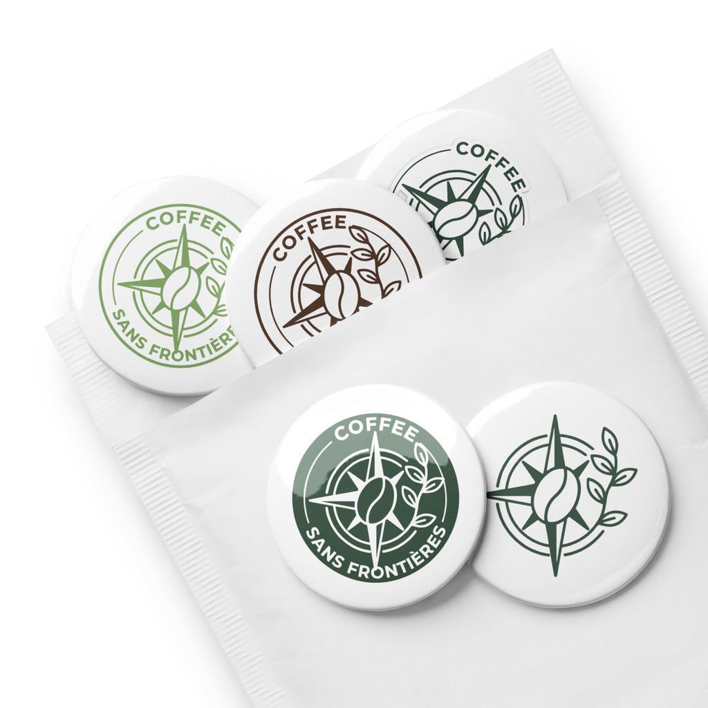 Four round white buttons with the Coffee Sans Frontières logo in green and brown, arranged on top of a white branded pouch.